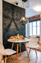 A dining area with a stone wall, a round table, white chairs, and a hanging light fixture.