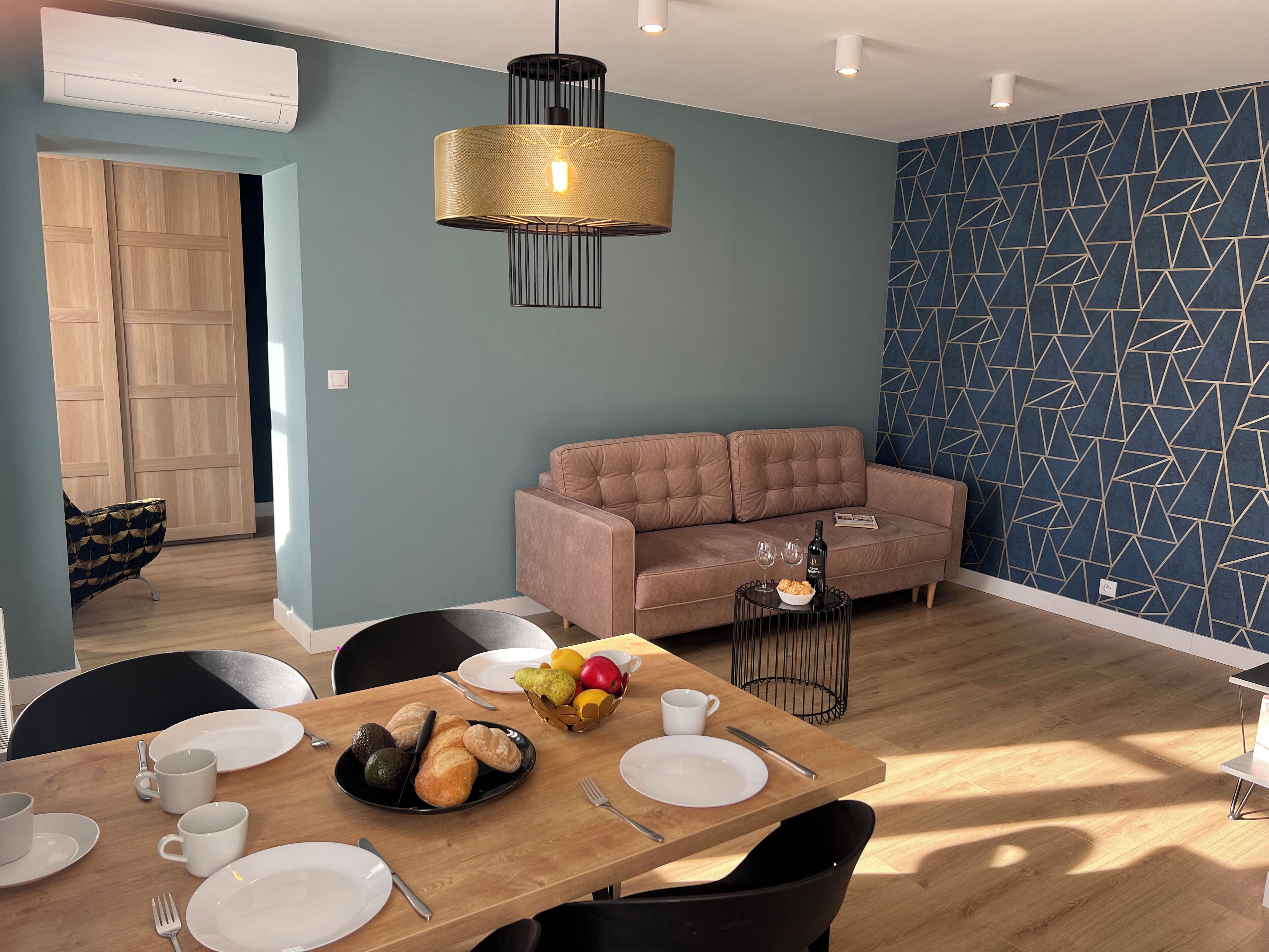 Un espace de repas moderne avec une table en bois dressée pour un repas, un canapé et un mur orné d’un motif géométrique.