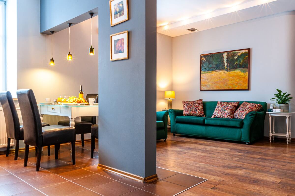 A modern living room with a green sofa, a dining area with chairs and a table, and a painting on the wall.