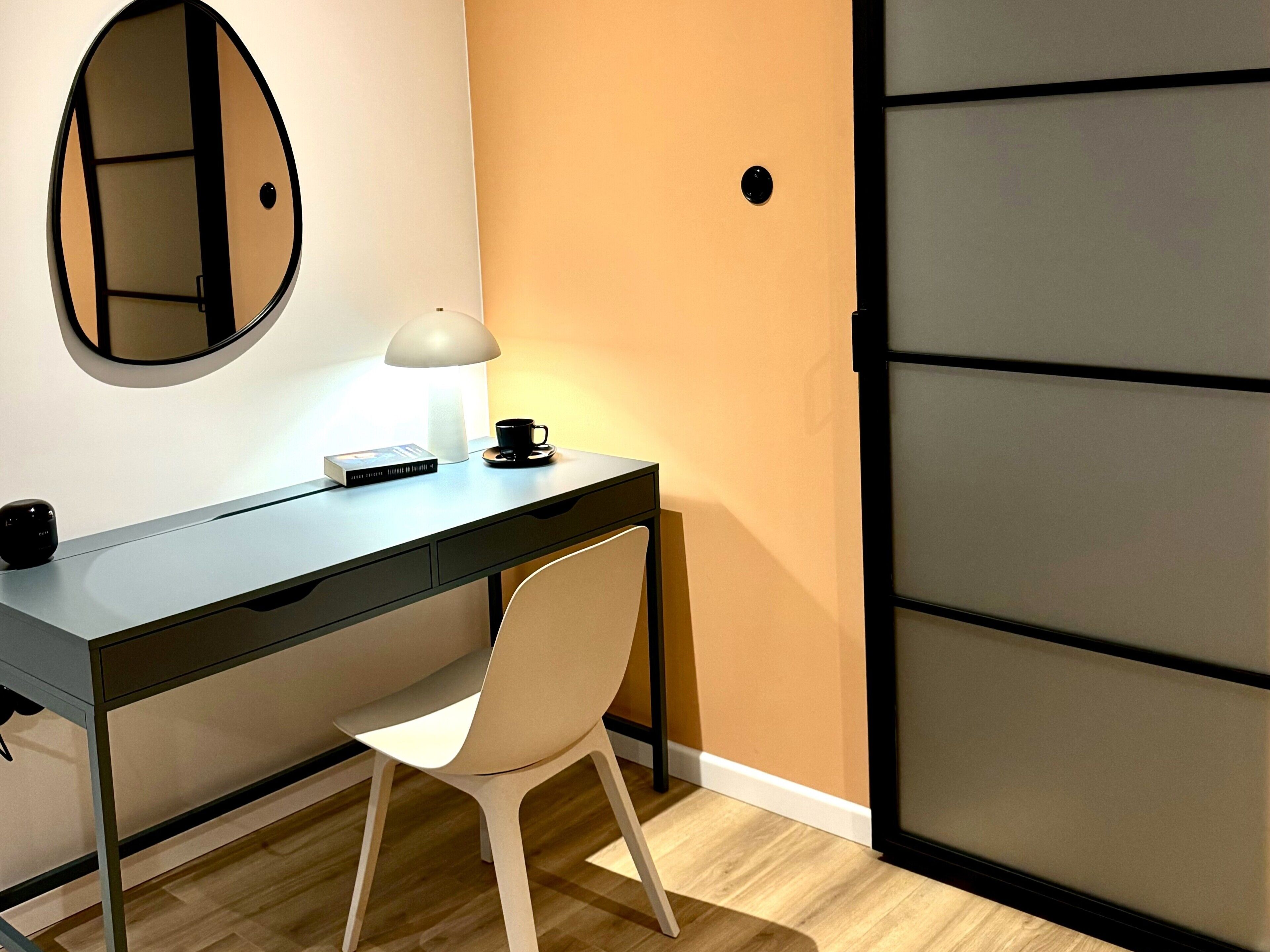 Een moderne kamer met een bureau, stoel, lamp en een spiegel.