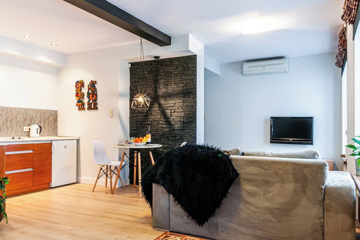 A modern living room with a stone accent wall, a flat-screen TV, a black furry ottoman, and a dining area with a small table and chairs.