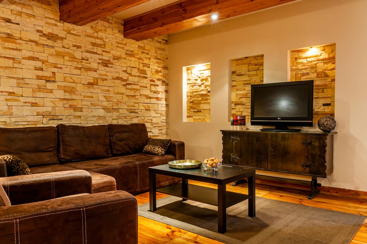A living room with a stone wall, a brown leather sofa, a wooden coffee table, and a television on a wooden cabinet.