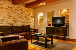 A living room with a stone wall, a brown leather sofa, a wooden coffee table, and a television on a wooden cabinet.