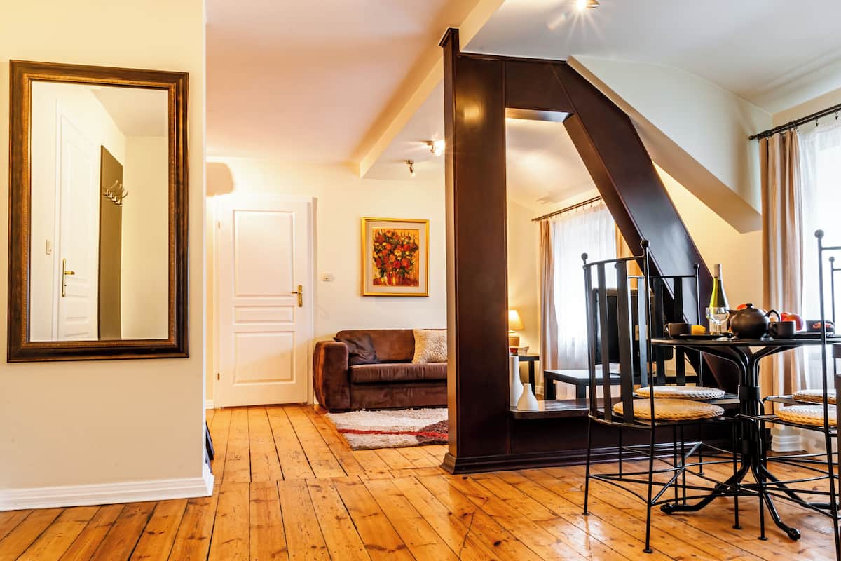 A cozy living room with a brown leather sofa, a dining table with chairs, and a staircase leading to another level.