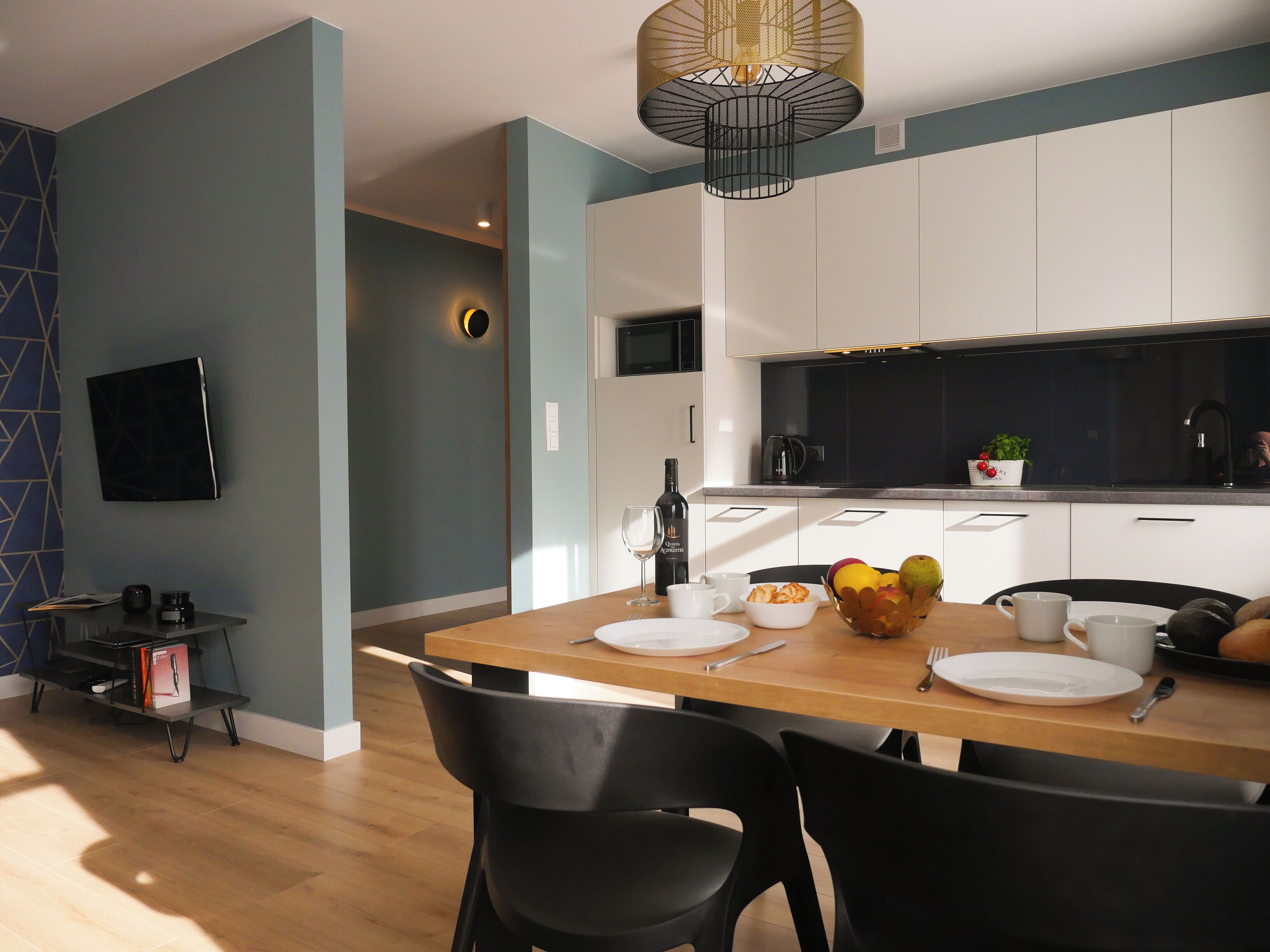 A modern kitchen with white cabinets, a black countertop, and a dining area with a wooden table and black chairs.