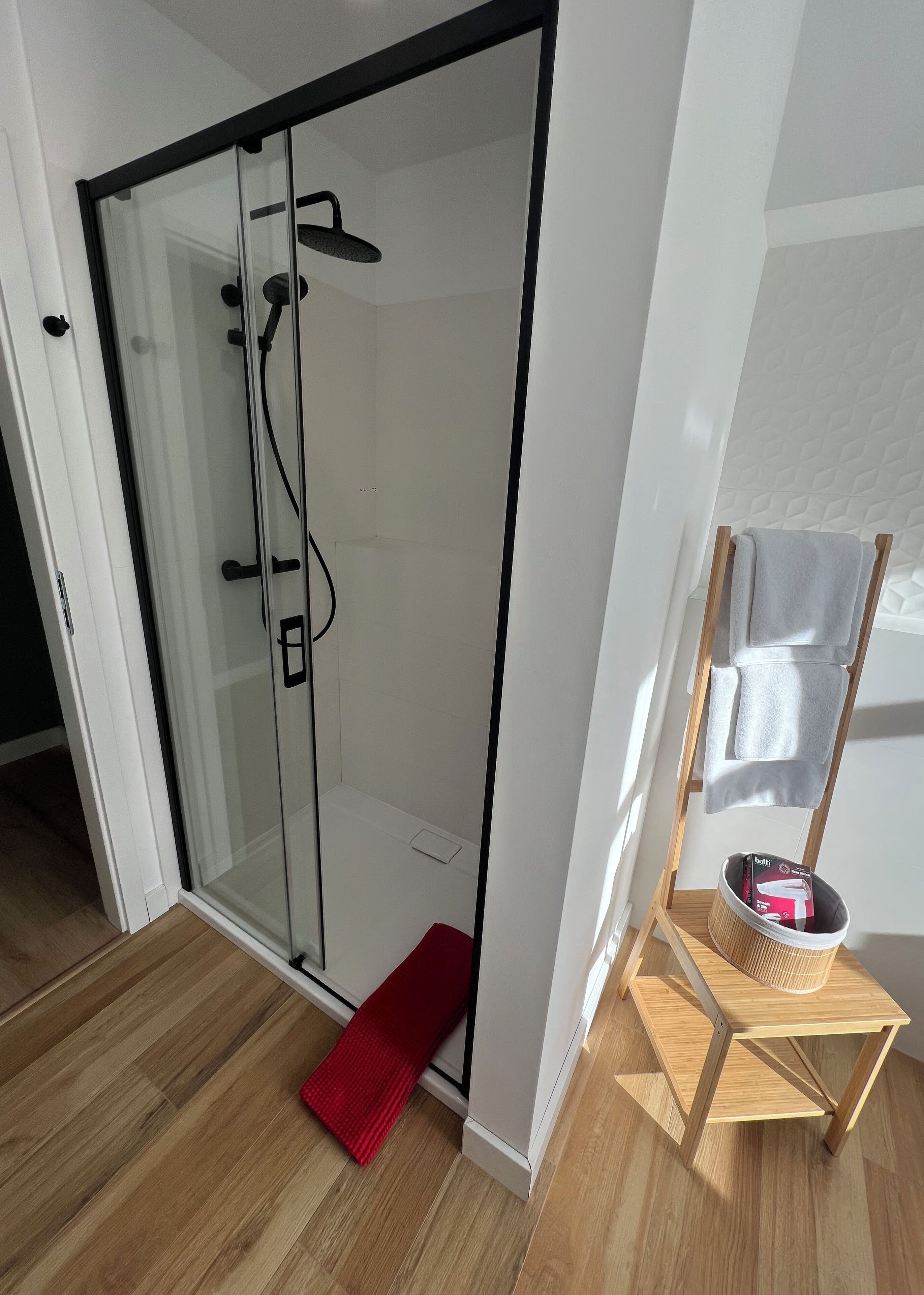 A modern bathroom with a glass shower enclosure, wooden flooring, and a towel rack with a towel.