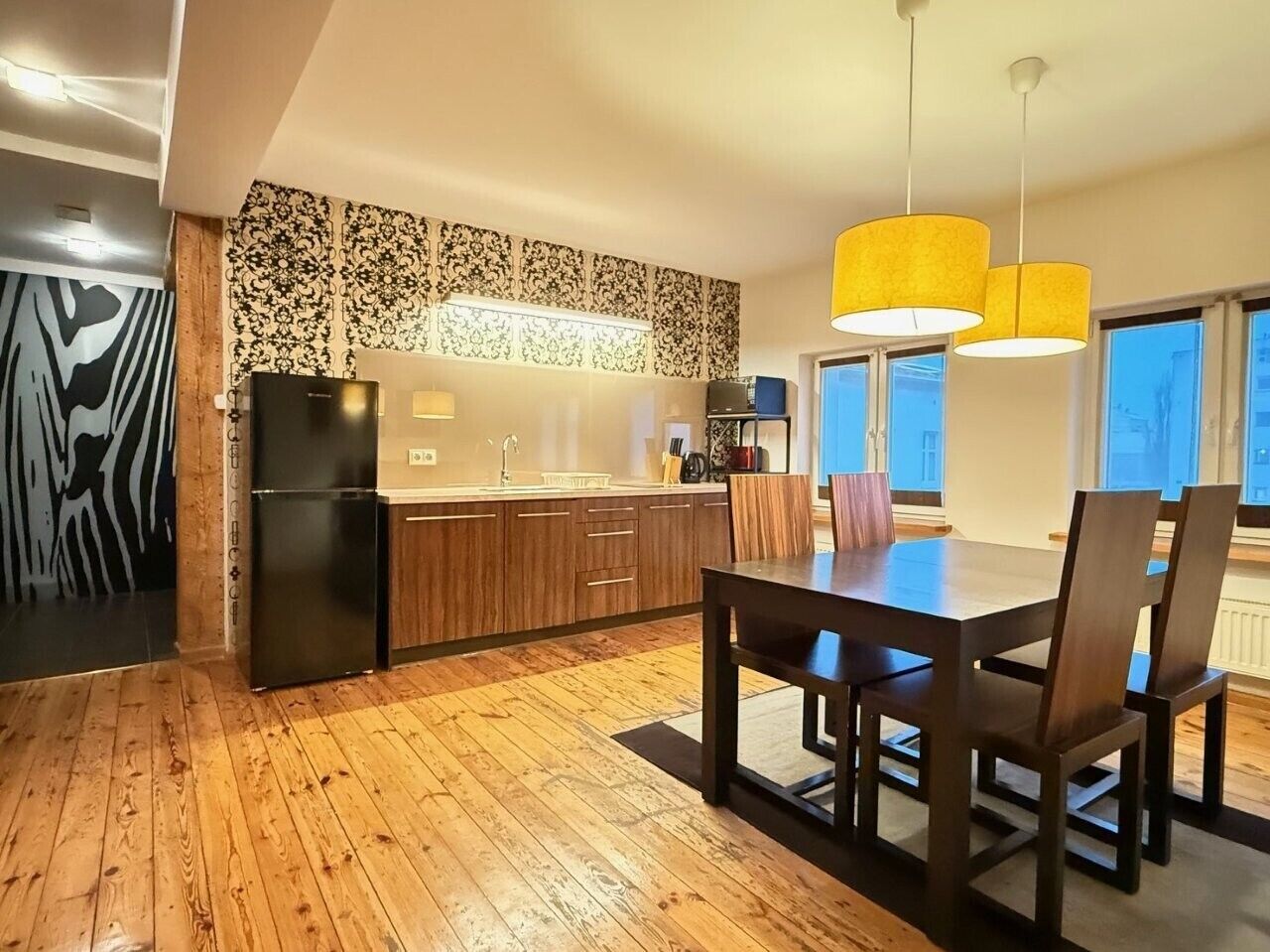 A modern kitchen with wooden flooring, a dining table with chairs, and a large window with a view.