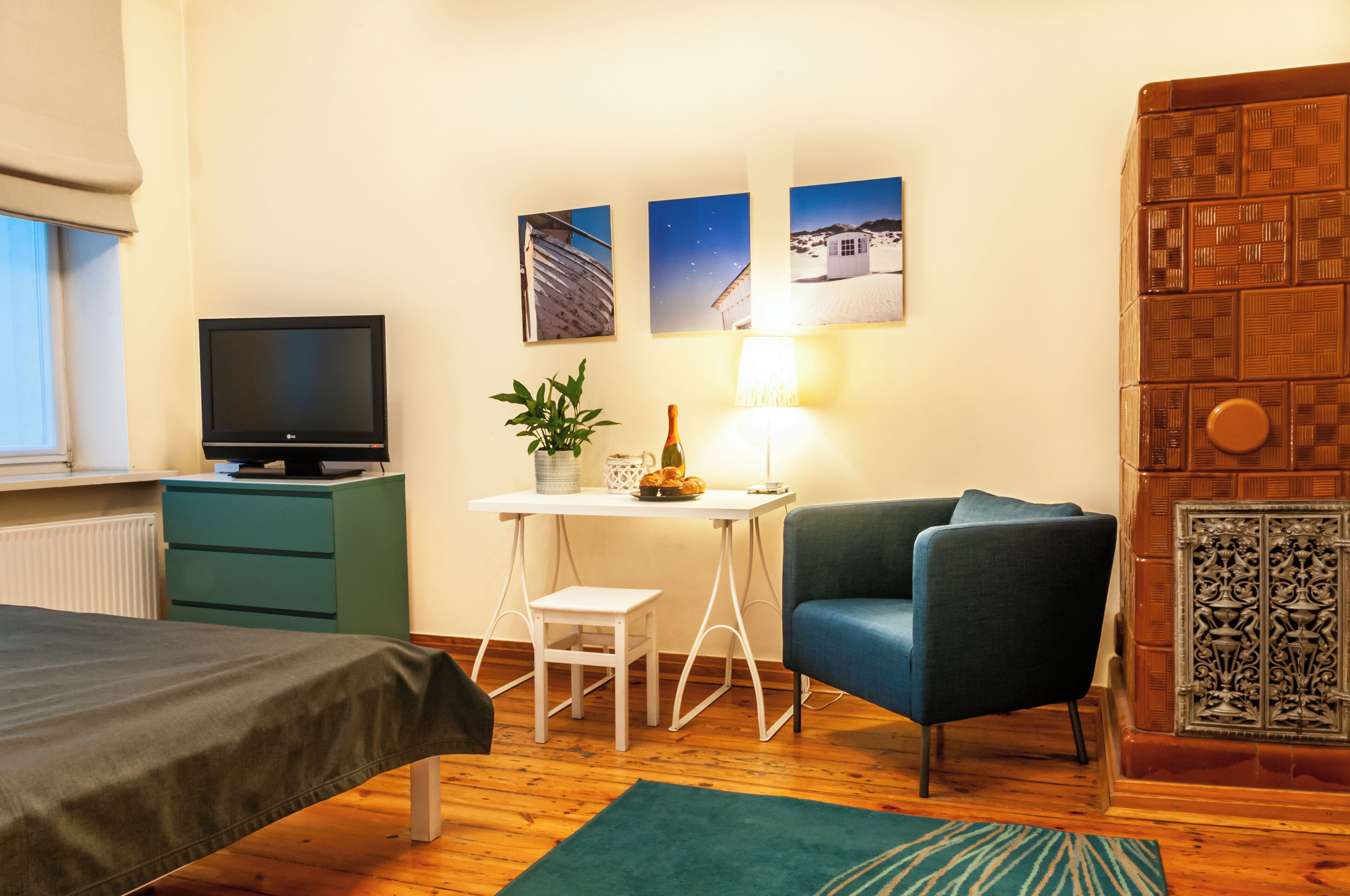 Une pièce comprenant un lit, un bureau avec un ordinateur, une chaise et un téléviseur. Trois tableaux encadrés sont accrochés au mur.