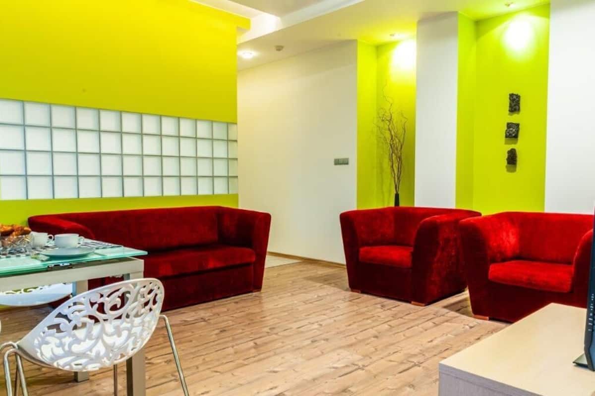A room with a bright yellow wall, a red sofa, a white chair, and a glass table with a white bowl and cups.