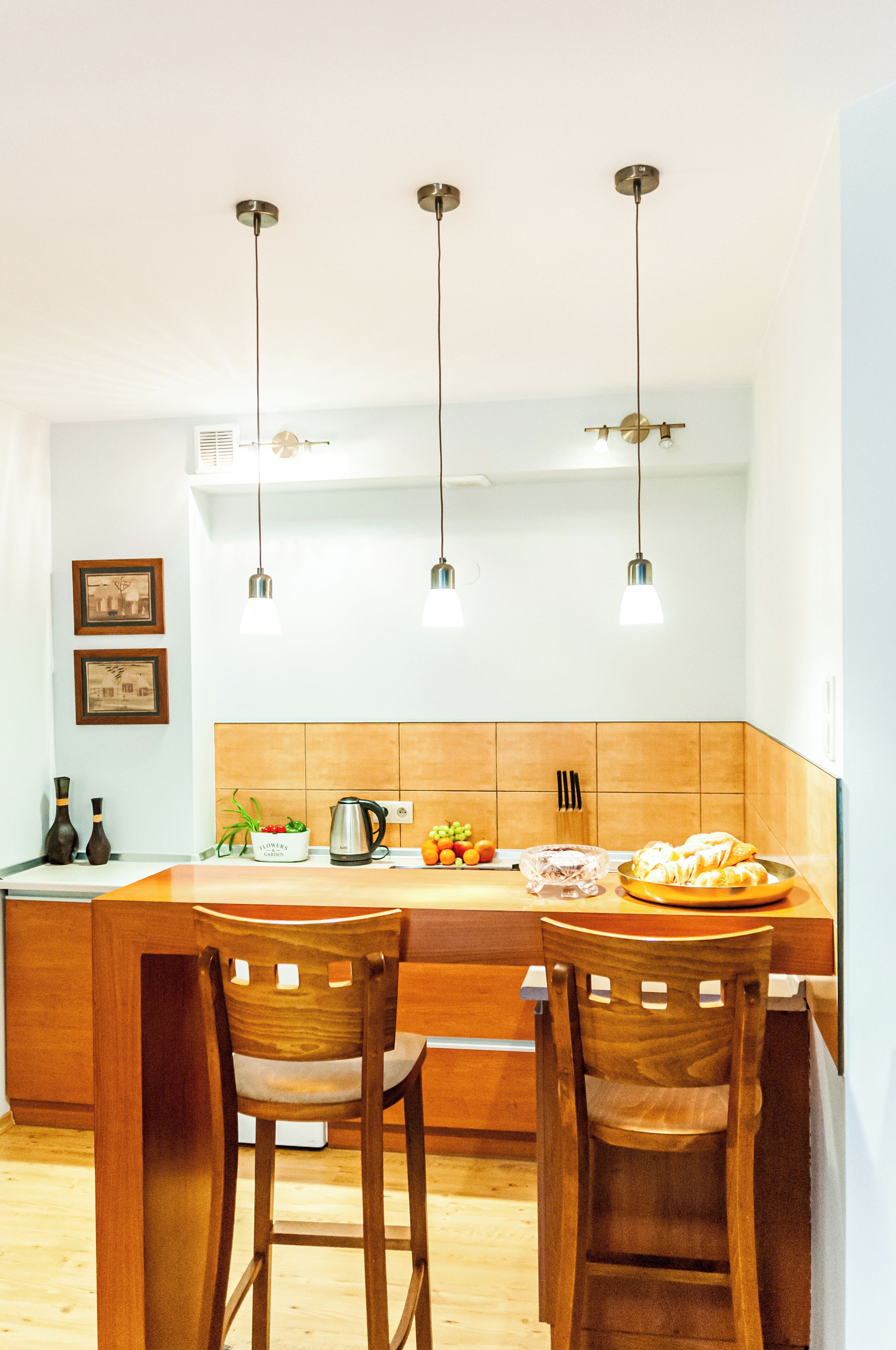 A modern kitchen with wooden chairs, pendant lights, and a central island.