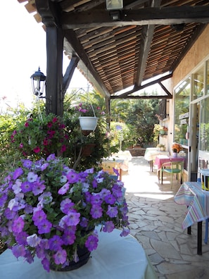 A covered outdoor area with tables and chairs, a reception desk, and potted plants. - Le Patio (Theoule-sur-Mer)