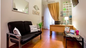 A living room with a black sofa, a coffee table, a desk with a computer, a TV, and a window with curtains. - Ottaviano Guest House (Rome)