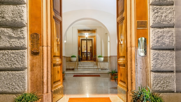 A grand entrance with a marble staircase leading to a door, flanked by potted plants and a plaque. - Ottaviano Guest House (Rome)