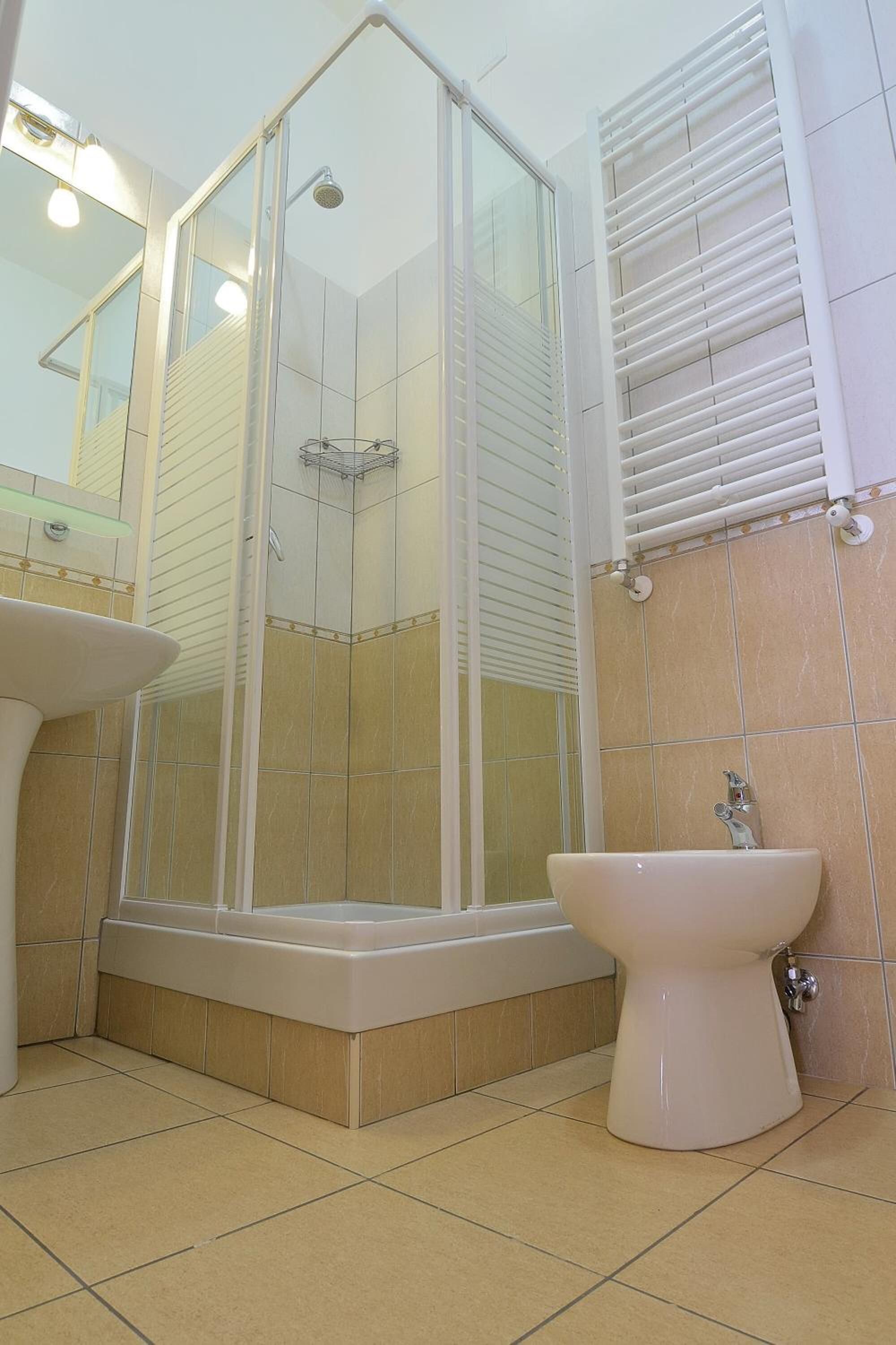 A modern bathroom with a glass-enclosed shower, a pedestal sink, and a toilet.