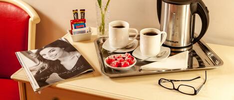 A tray with two cups of coffee, a coffee pot, a bowl of snacks, a magazine, a pair of glasses, and a vase with flowers.