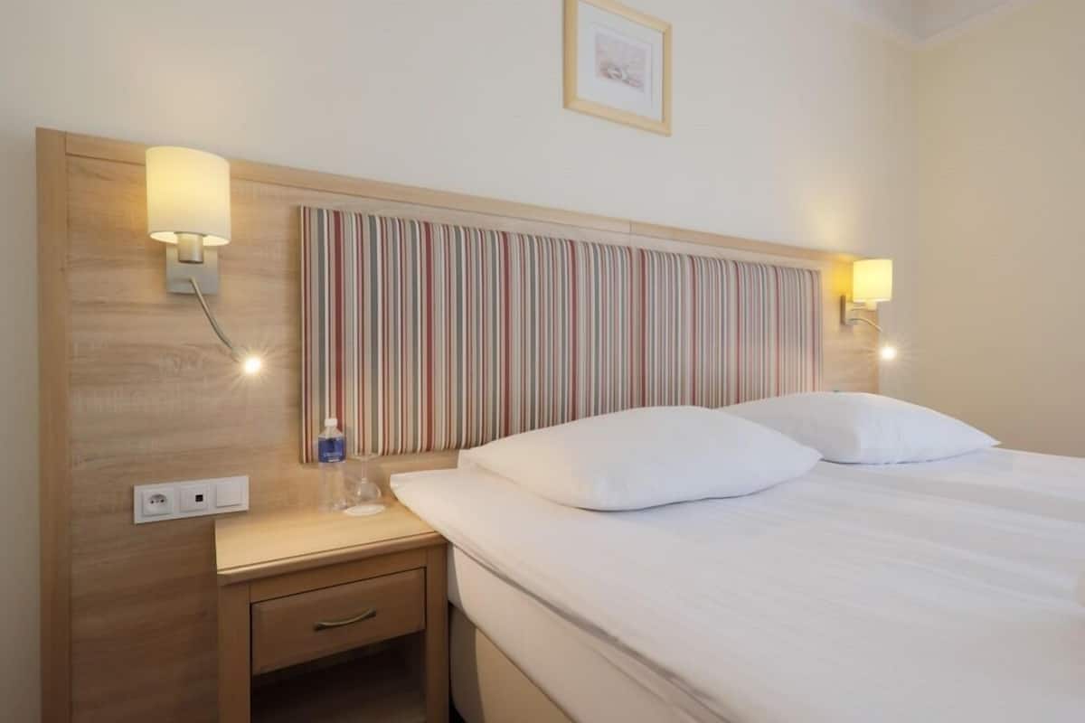 A hotel room with a striped headboard, bedside lamps, a bedside table with a bottle, and a framed picture on the wall.