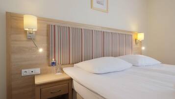 A hotel room with a striped headboard, bedside lamps, a bedside table with a bottle, and a framed picture on the wall.