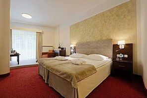 A hotel room with a bed, bedside tables, a lamp, a nightstand, a chair, a desk, and a window with curtains. - Papuga Park Hotel Wellness Marrakesz & SPA (Bielsko-Biala)