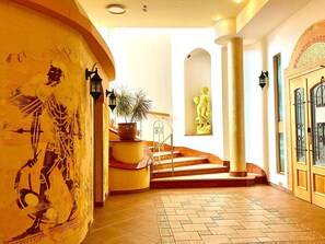 Un vestíbulo de hotel con una escalera, una planta en maceta, una estatua y un mural en la pared.