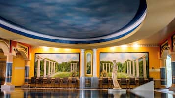 A pool area with a mural of columns and a statue, seating, and a ceiling with a painted sky.