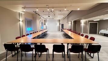 A conference room with a long table and chairs, equipped with ceiling lights and a whiteboard.