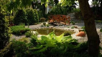 Een tuin met een vijver, een houten brug en diverse planten.