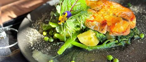 A plate of food with a piece of grilled meat, vegetables, and a flower garnish.