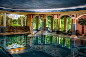 Un área de piscina con una estatua, sillas de descanso y un mural de columnas antiguas.