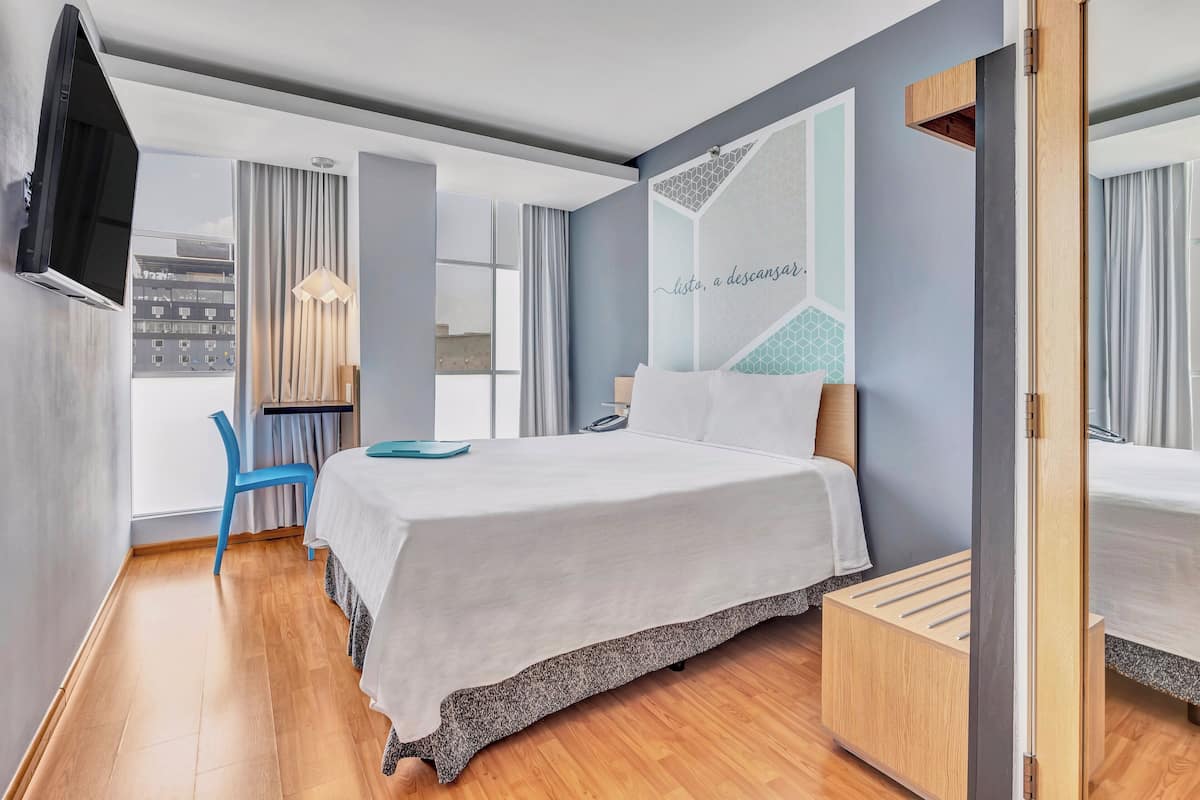 Ein modernes Hotelzimmer mit einem großen Bett, einem Schreibtisch und einem an der Wand befestigten Fernseher.