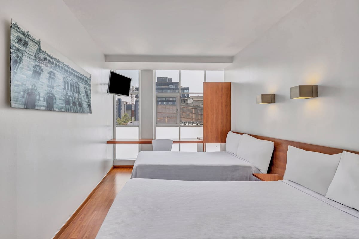 Ein modernes Hotelzimmer mit einem großen Bett, einem an der Wand montierten Fernseher und Blick auf die Stadt durch das Fenster.