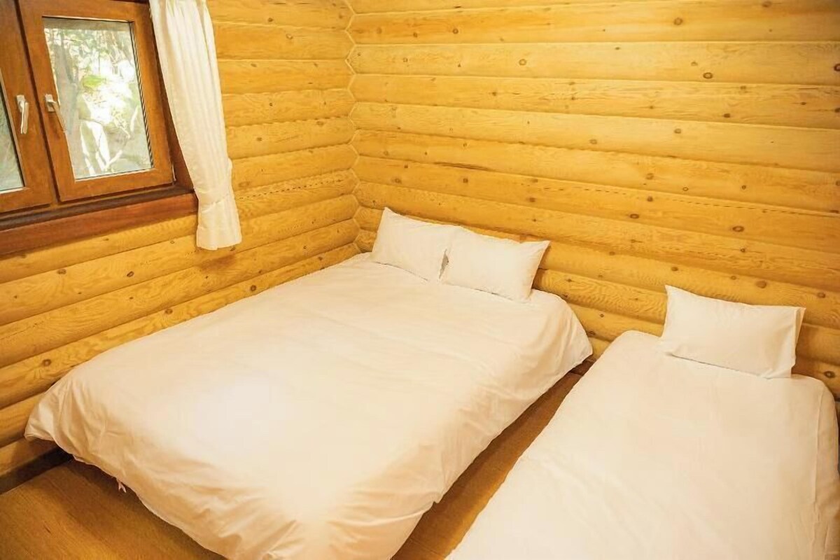 Une chambre dans un chalet en bois, avec deux lits, une fenêtre avec des rideaux et un plancher en bois.