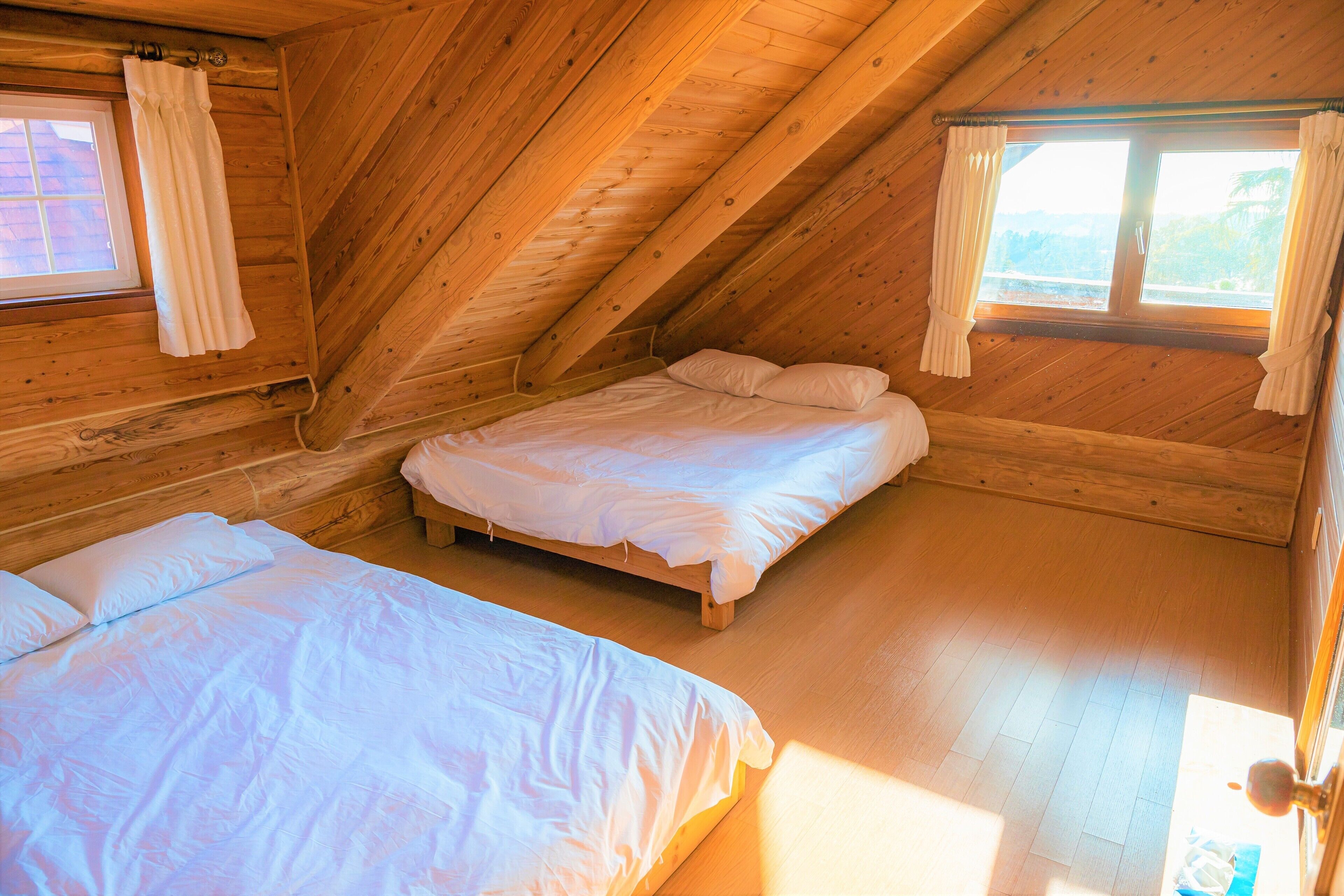 A wooden cabin with two beds, a window with curtains, and a sloped ceiling.