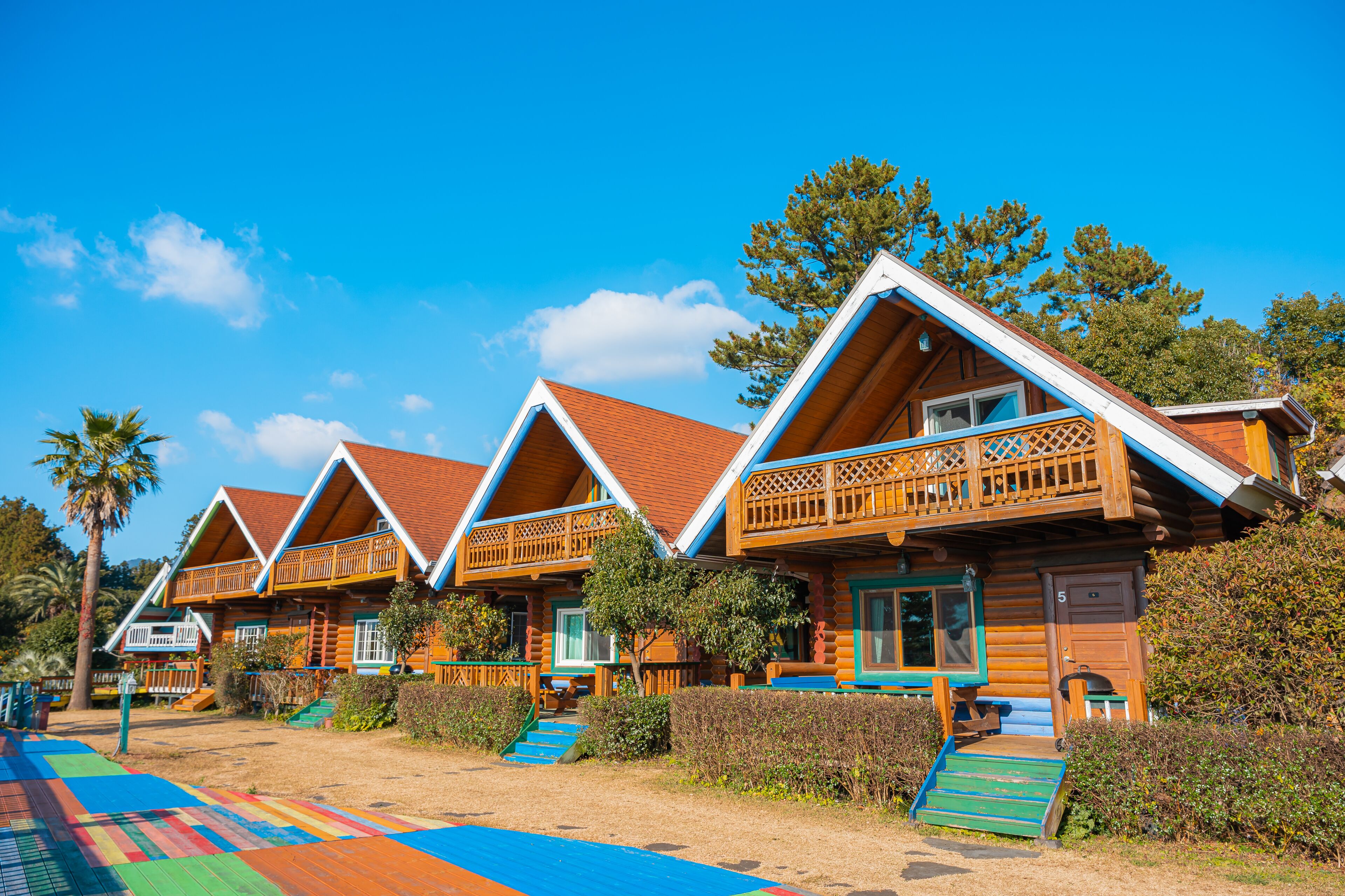 A row of log cabins with wooden balconies, a colorful carpet, and a clear blue sky.
