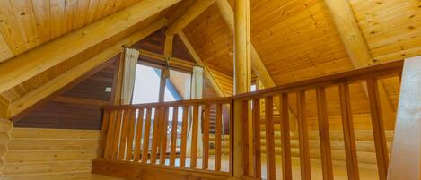 A wooden interior with a balcony, wooden beams, and a ceiling fan.