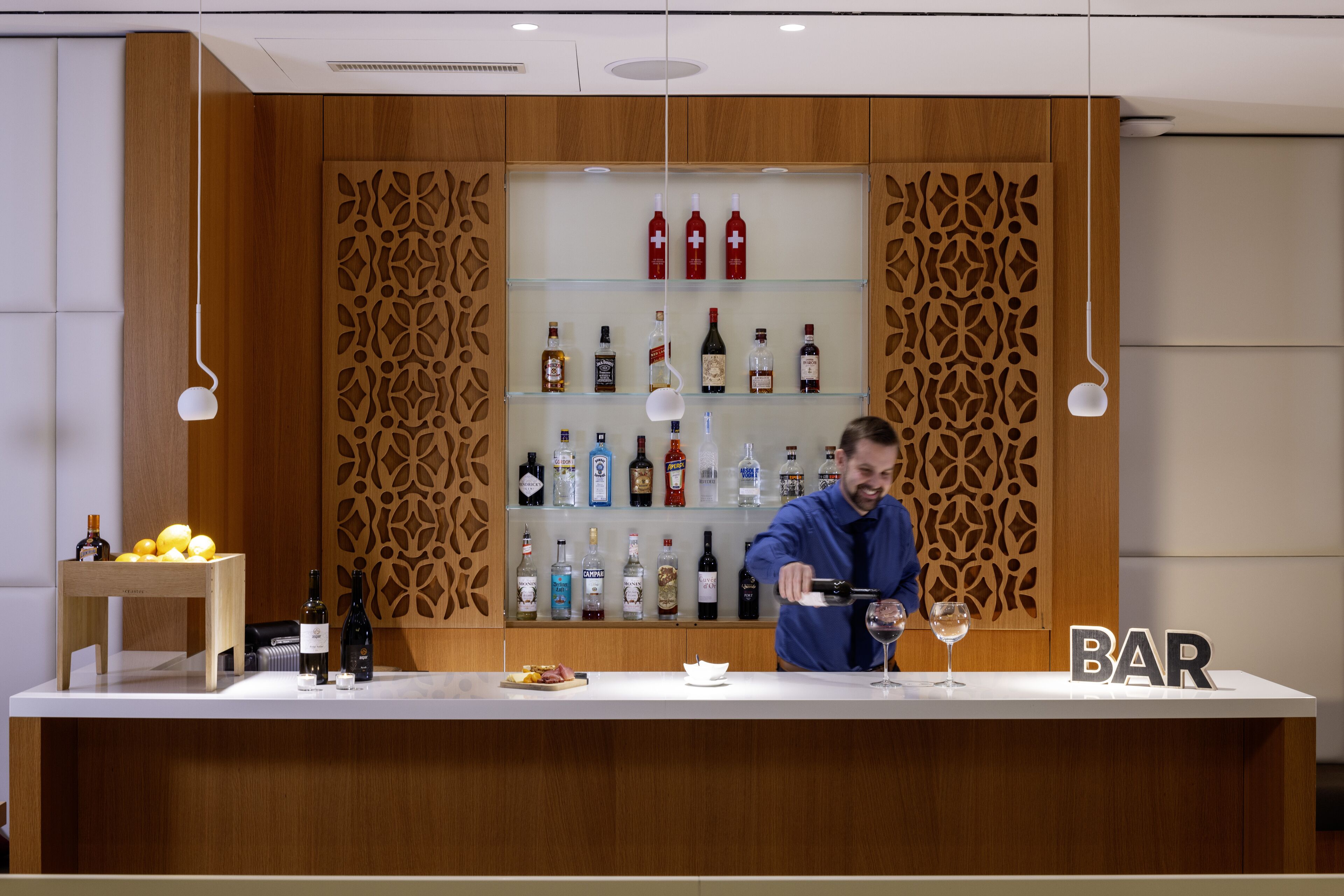 A bar area with a wooden panel design, shelves with various bottles, and a counter where a person is pouring a drink.