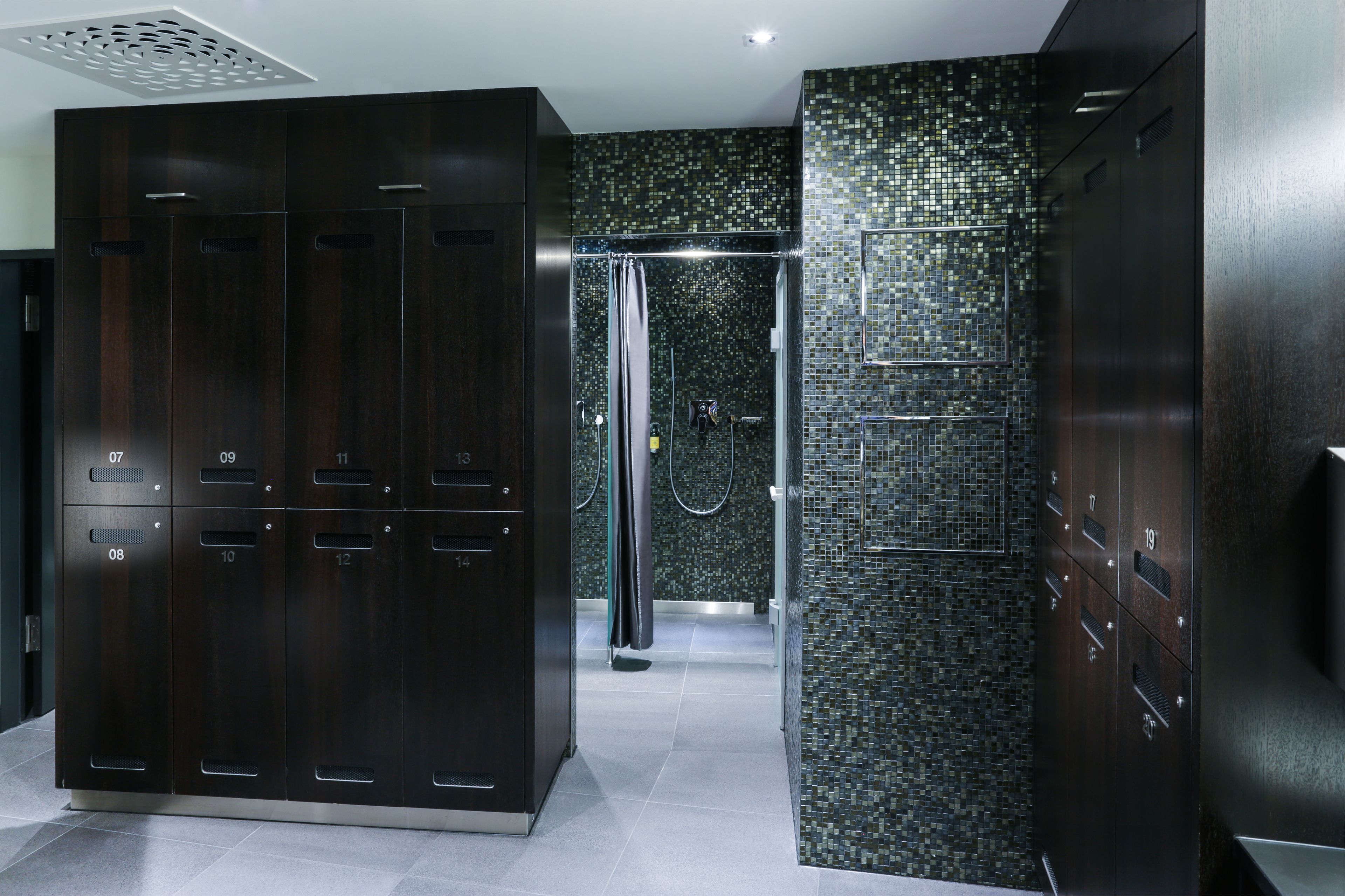 A modern bathroom with dark wood lockers, a glass shower enclosure, and a mosaic tile wall.