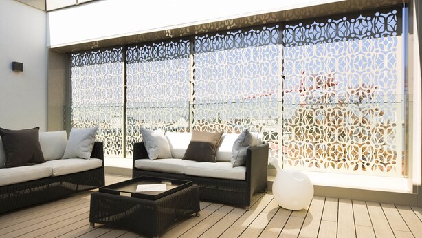 A modern outdoor seating area with two sofas and a coffee table, separated by a decorative screen.
