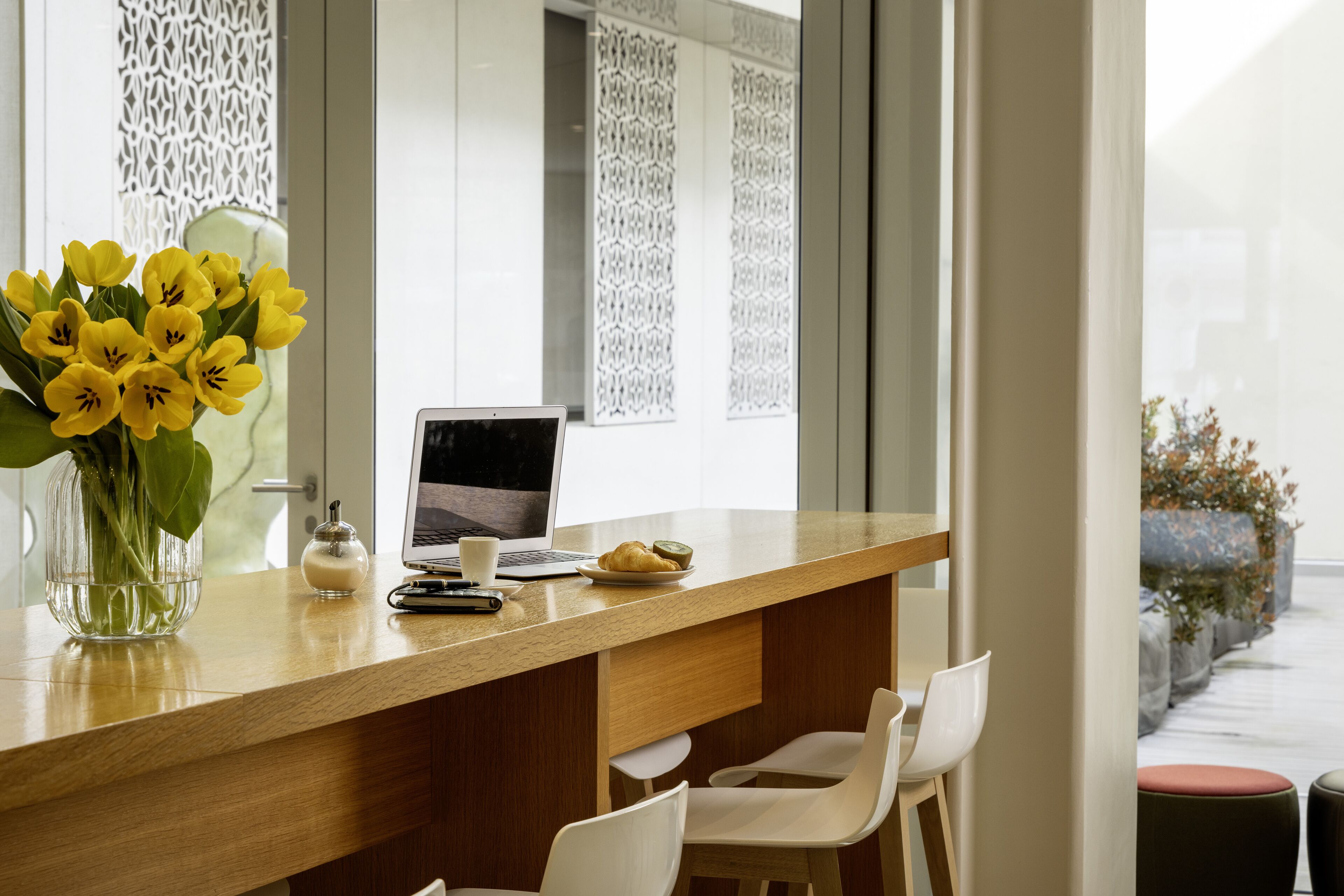 Et moderne køkken med en træbordplade, en bærbar computer, en vase med gule blomster og en kaffekop.