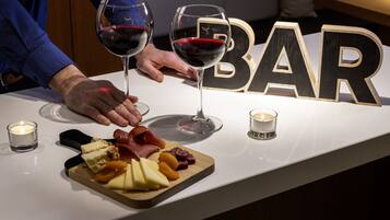 Um bar com uma tábua de madeira de queijos e charcutaria, dois copos de vinho tinto e velas sobre a mesa.