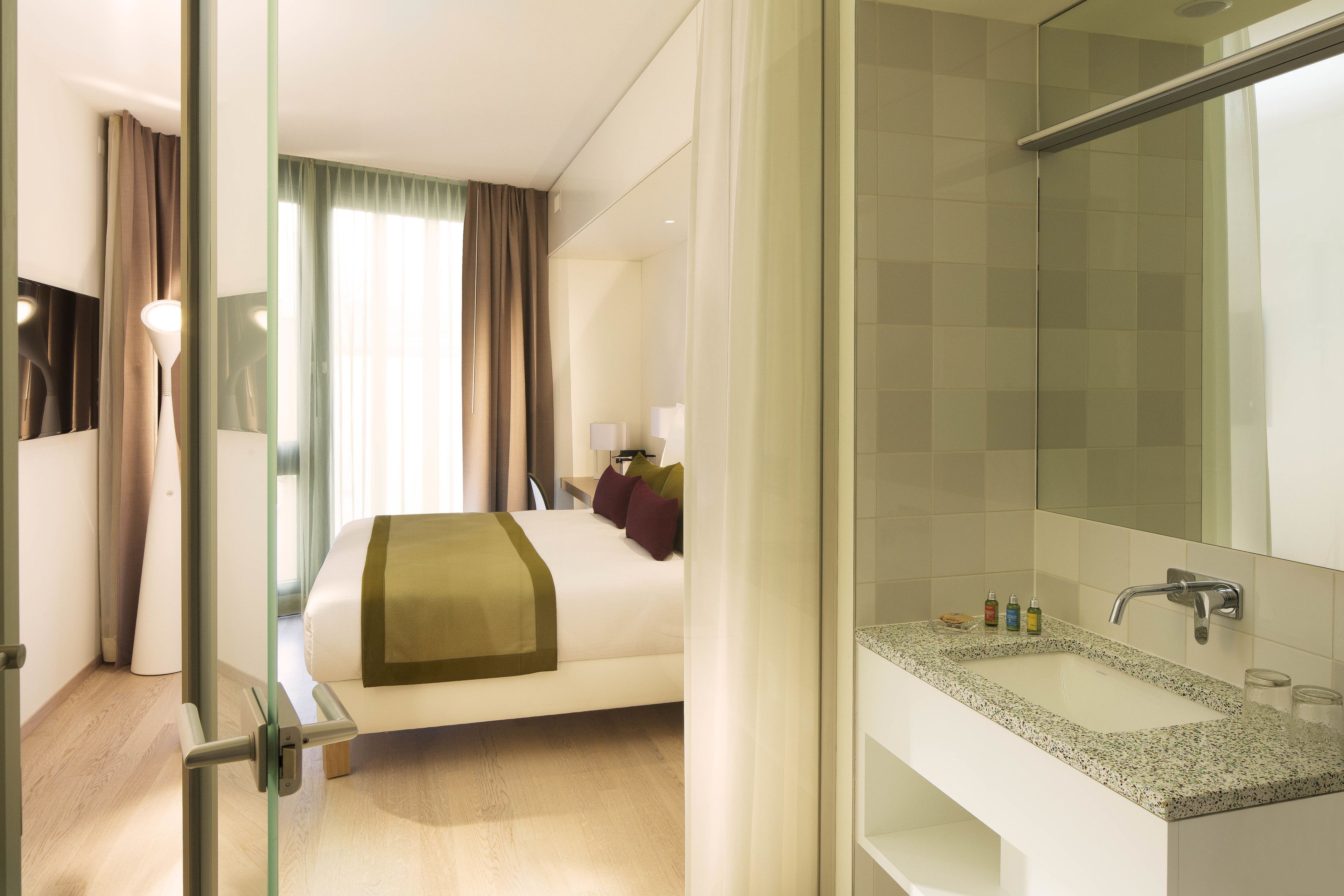 A hotel room with a bed, a bathroom with a sink and mirror, and a shower area.