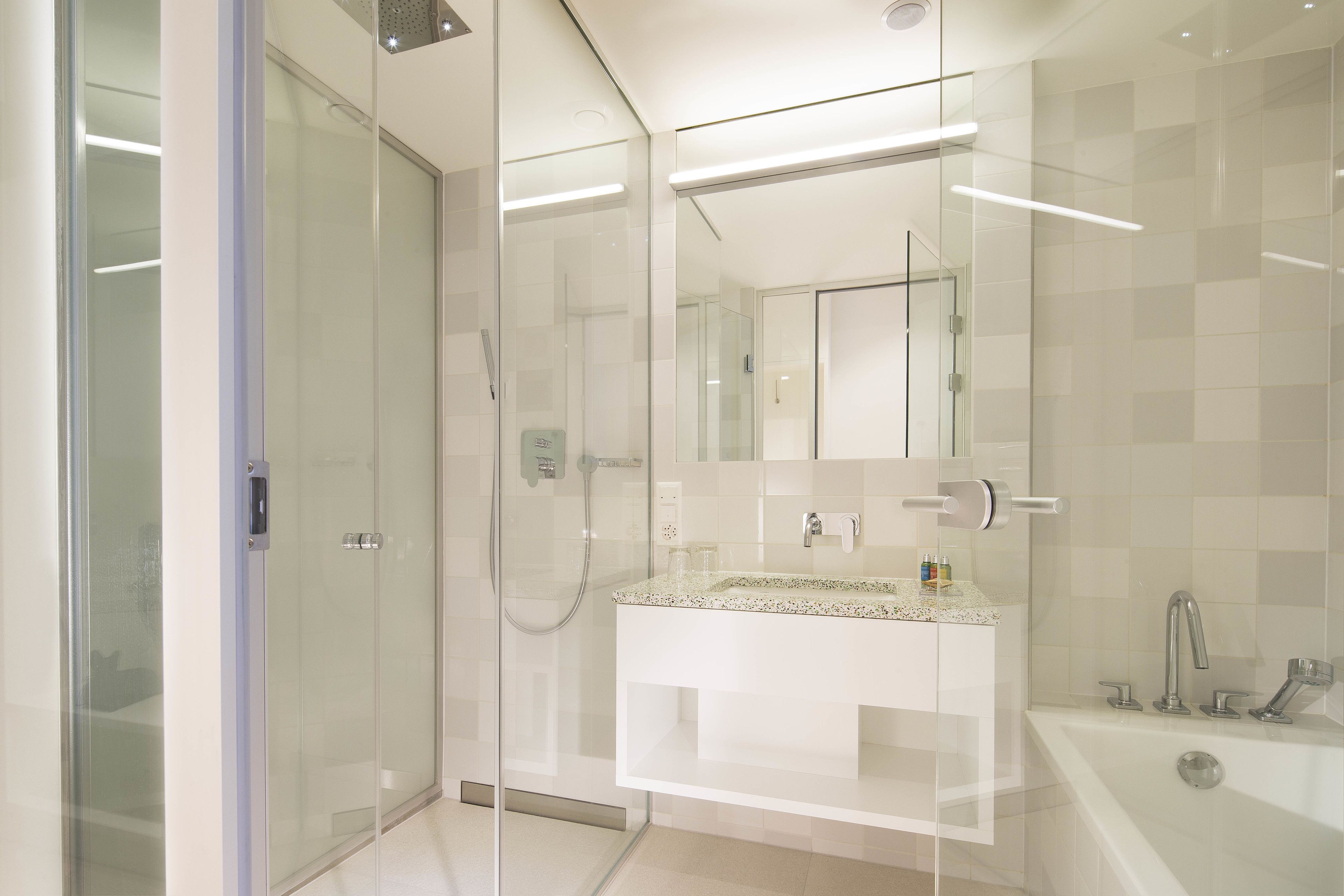 Une salle de bain moderne dotée d’une douche à parois de verre, d’un meuble-lavabo blanc avec un plan de travail en granit et d’une baignoire îlot.