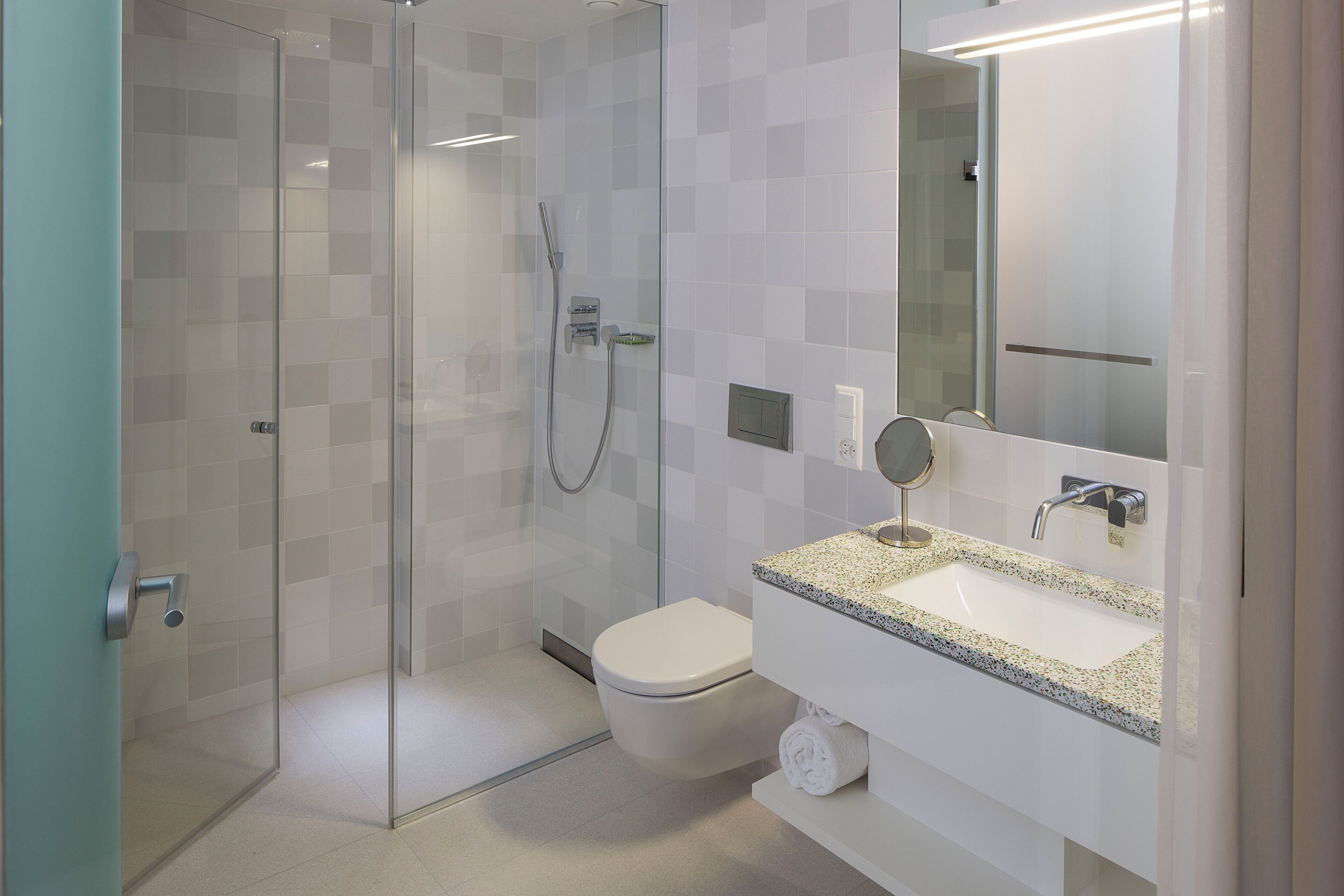 A modern bathroom with a glass-enclosed shower, a white toilet, a granite countertop sink, and a mirror above the sink.