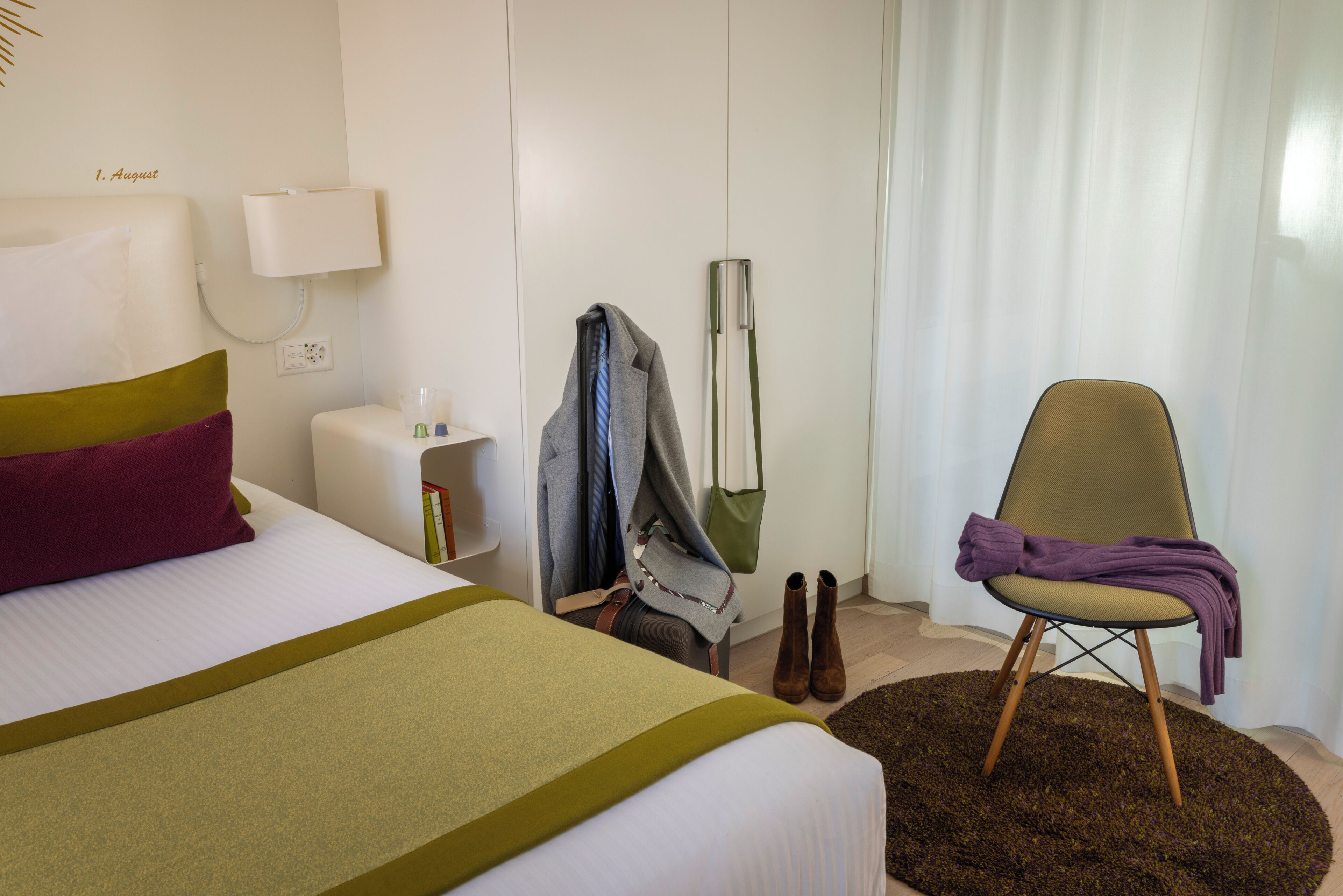 Una habitación de hotel con una cama, una silla, perchero y una lámpara.
