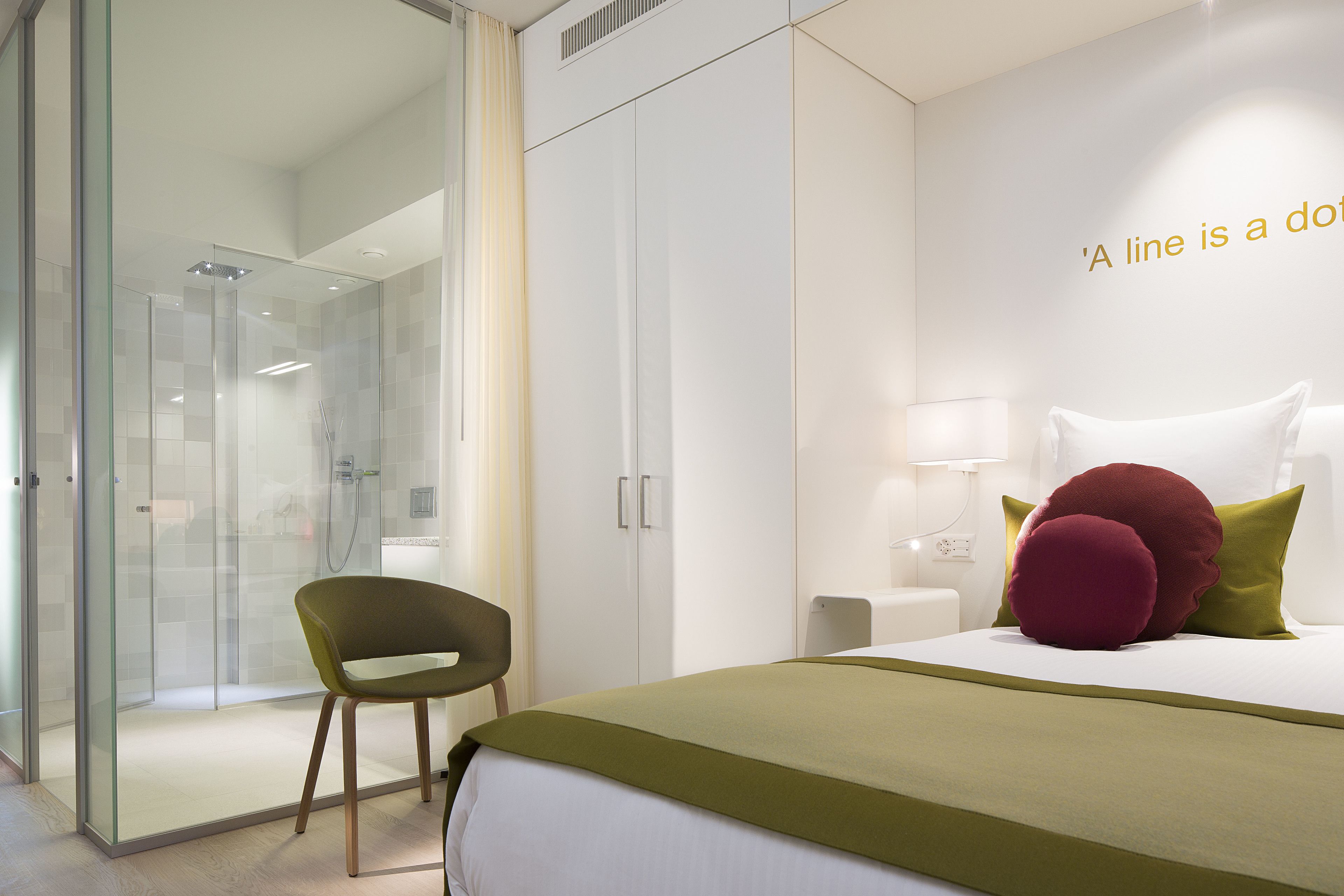Une chambre d’hôtel moderne dotée d’une douche en verre, d’un lit simple avec une literie verte et d’une chaise verte.