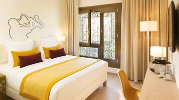 A hotel room with a bed, a desk, a chair, a window with curtains, and a wall decoration.