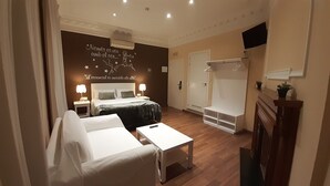 Une chambre d’hôtel comprenant un lit, des tables de chevet, un bureau, une chaise, un peignoir, un espace douche et un téléviseur fixé au mur.