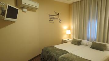 A hotel room with a bed, a desk with a lamp, an air conditioner, and a wall decoration.