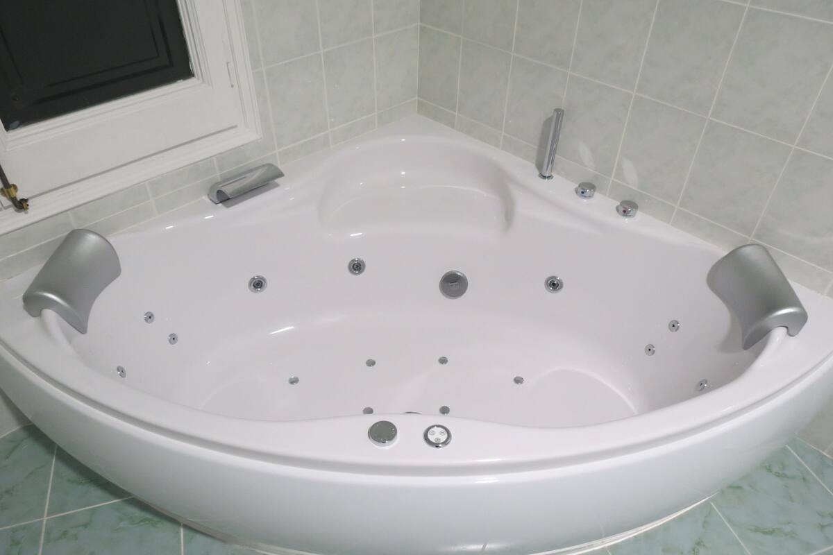 A large, oval-shaped bathtub with multiple jets, a handheld showerhead, and a built-in seat.