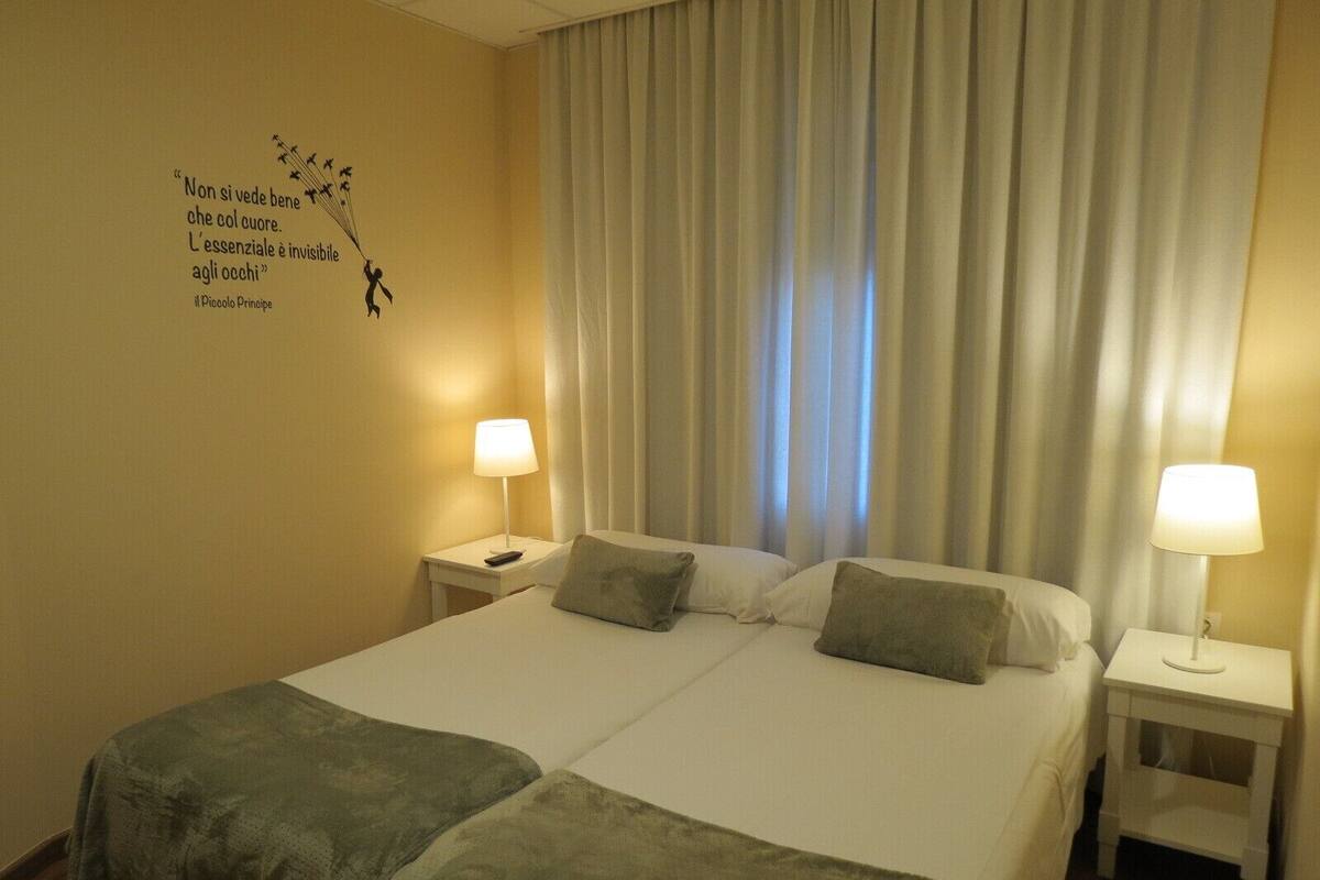 A hotel room with a large bed, two bedside tables, and a wall quote.