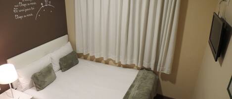 A hotel room with a bed, a nightstand, a lamp, a TV, and a wall with a motivational quote.